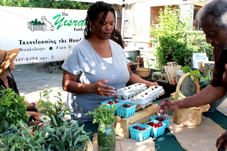 Judith Yisrael sells produce to her father-in-law, Hal, during the first farm stand at Yisrael Family Urban Farm in Sacramento in May. (Photo by Sena Christian)
