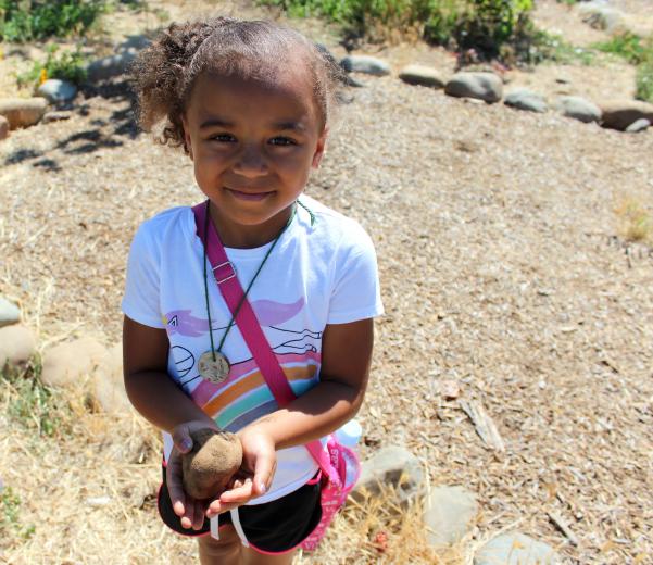A child participating in Soil Born's summer day camp holds up a potato uncovered in the soil. These weeklong camps are popular and fill up well in advance, says Youth Education Coordinator Alyssa Kassner. (Photo by Sena Christian)