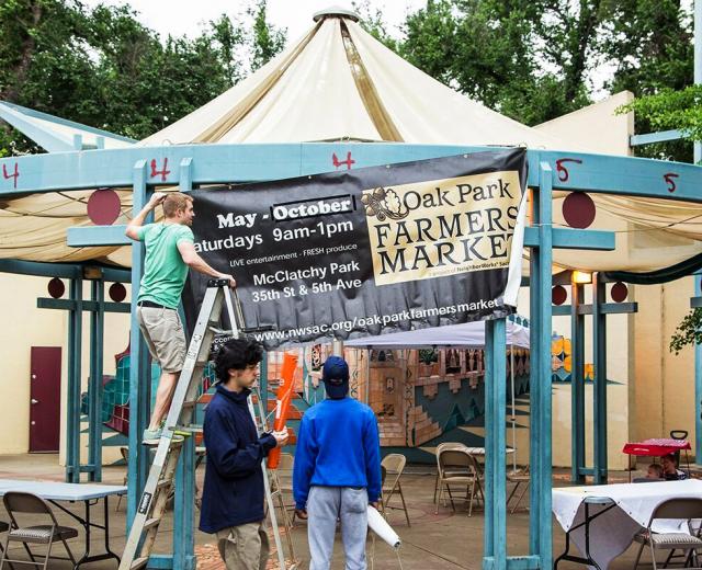 Luke Spates, of NeighborWorks Sacramento, raises the banner for the Oak Park Farmers Market as it opens its seventh season in McClatchy Park.
