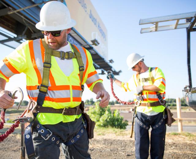 Safety comes first for billboard crew members Rick Barton (left) and Daniel Stutes (right), of Outfront Media, as they change out a billboard along Capital City Freeway in Sacramento. New employees undergo hands-on climbing training, which covers harness safety and personal protective equipment training; everyone has annual classroom study