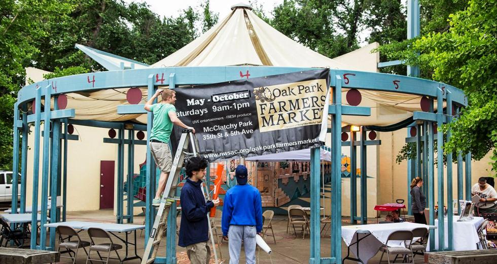 Luke Spates, of NeighborWorks Sacramento, raises the banner for the Oak Park Farmers Market as it opens its seventh season in McClatchy Park.
