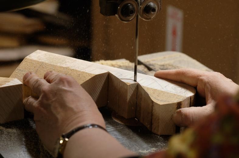 She repairs an old viola as shop helper Tim Winters outlines the shape of a new violin on a piece of wood.