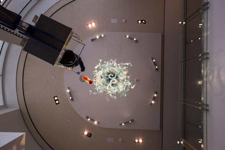 As Jessie Svozil uses a duster on each individual piece of the “Golden Teal Chandelier” hanging from the lobby ceiling in the Crocker Art Museum, the sculpture moves ever so slightly.