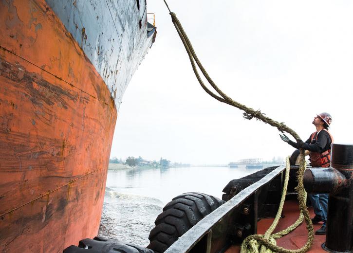 Here, Brusco Tug & Barge deckhand Artie Menosse tightens a line of rope connecting the two ships so the tugboat can guide the larger vessel to shore. “A majority of these ships can stop, but they can’t go sideways or go back and turn, so we put a line on and help guide them into the dock,” says Captain Jeff Hedlund.
 Here, Brusco Tug & Barge deckhand Artie Menosse tightens a line of rope connecting the two ships so the tugboat can guide the larger vessel to shore. “A majority of these ships can stop, but they can’t go sideways or go back and turn, so we put a line on and help guide them into the dock,” says Captain Jeff Hedlund.