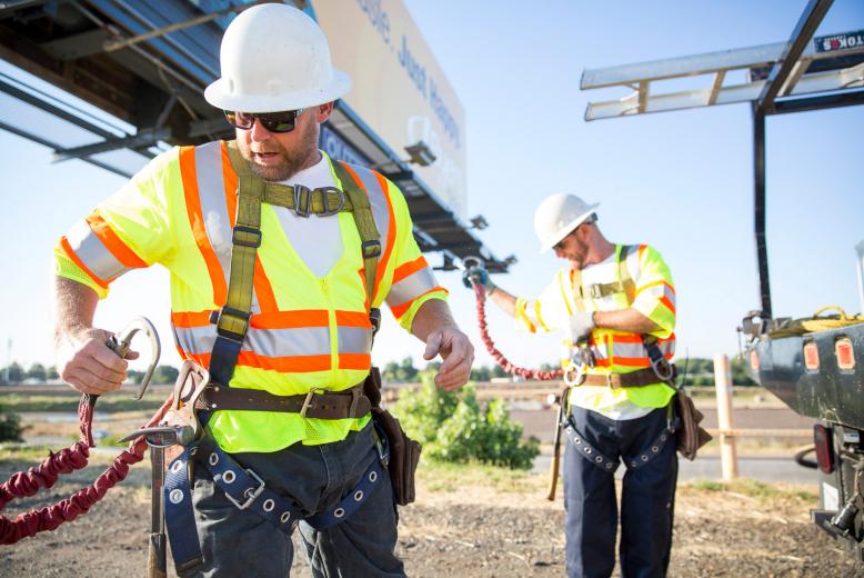 Safety comes first for billboard crew members Rick Barton (left) and Daniel Stutes (right), of Outfront Media, as they change out a billboard along Capital City Freeway in Sacramento. New employees undergo hands-on climbing training, which covers harness safety and personal protective equipment training; everyone has annual classroom study