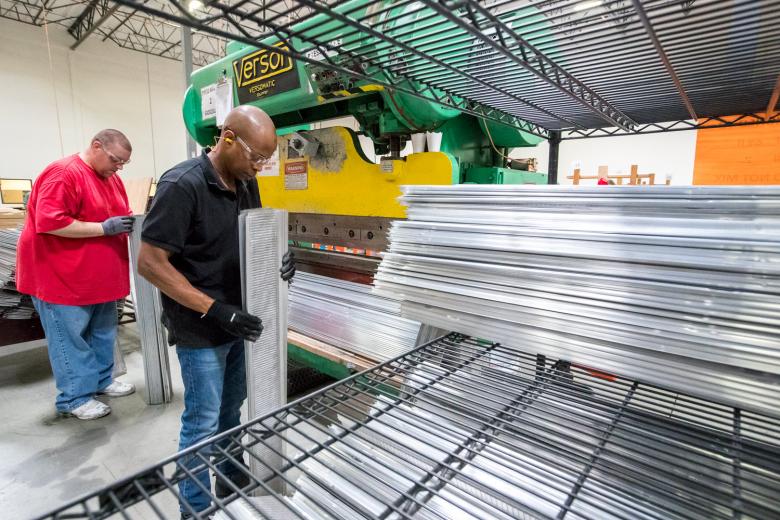 Zac Epling (left) and Boubacar Sy Savane next place the pre-assembled gutter guards into a press before they are boxed as a DIY kit sold to retailers, including Home Depot and Costco.