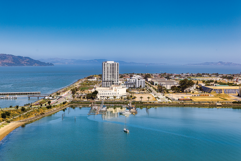 A bird’s-eye view of Treasure Island from adjoining Yerba Buena Island showcases Isle House, a 22-story, 250-unit residential building that opened in September 2024 and was the island’s first high-rise. (Photo by Steve Martarano)