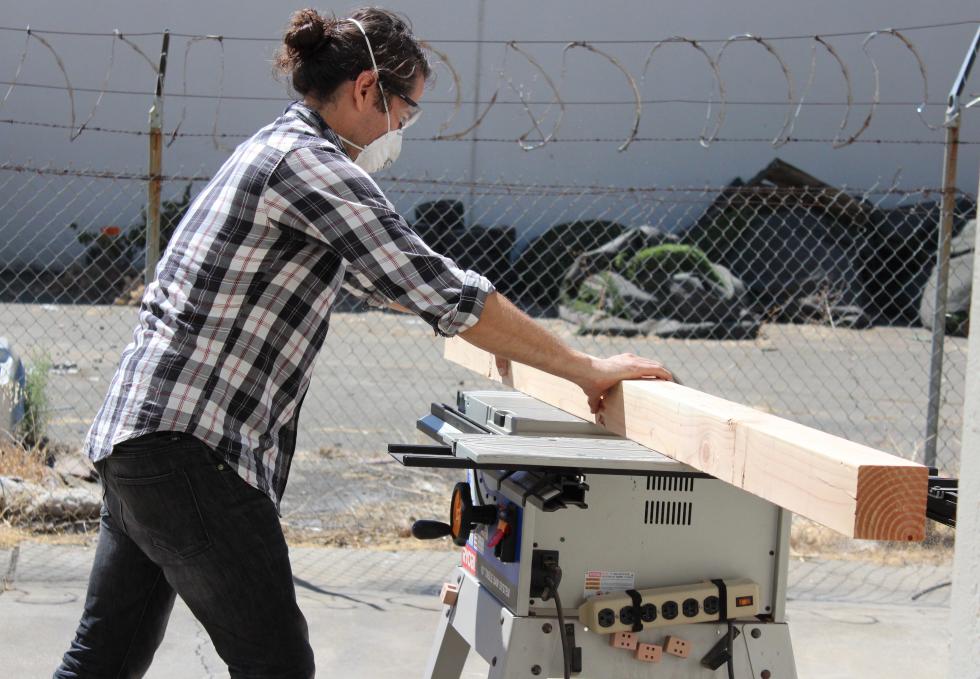 Bryan Valenzuela saws wood to create a table as part of the prep work in a Sacramento warehouse for his sculpture, “Multitudes Converge.”