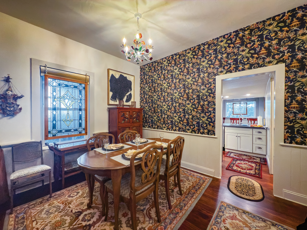 The dining room highlights a shared family legacy. Stained glass by Mickey Abbey hangs above an antique tea cart handmade by Rebekah Christensen’s grandfather. Rebekah herself painted the chandelier, once owned by Keith Christensen’s mother, to echo the colors in the East Asian-inspired wallpaper. Framed art features Rebekah’s great-grandmother’s shawl and fan.